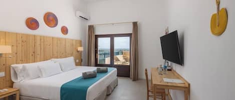 A hotel room with a bed, a desk, a TV, and a view of the sea.