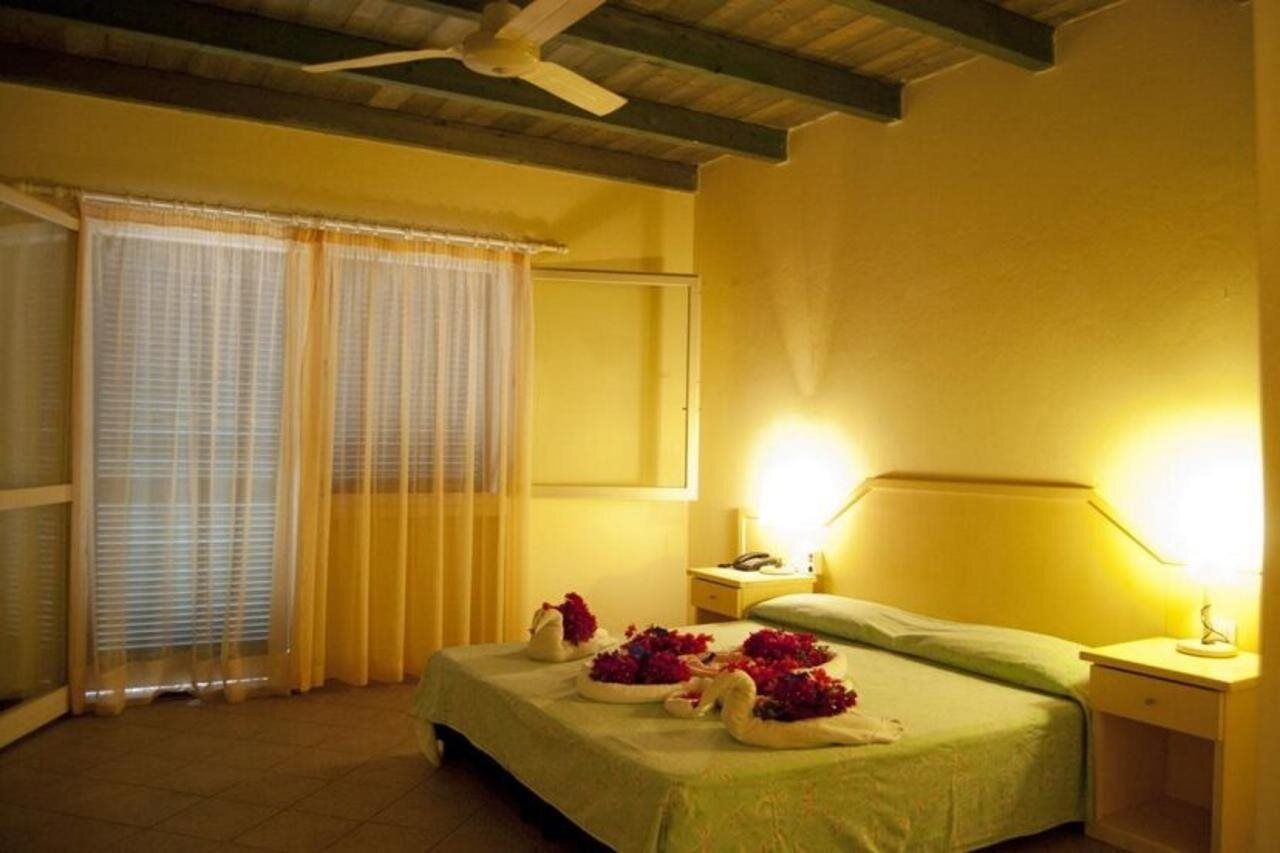 A hotel room with a bed, a bedside table, a nightstand, a ceiling fan, and curtains.
