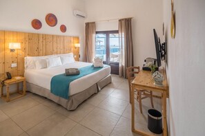 Une chambre d’hôtel comprenant un lit, des tables de chevet, un bureau avec une chaise, une fenêtre avec des rideaux et une vue sur la mer.