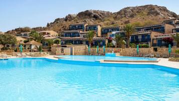 A swimming pool with lounge chairs, a mountain backdrop, and buildings with blue accents.