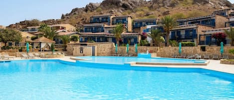 Una piscina con sillas de descanso, montañas al fondo y edificios con detalles azules.