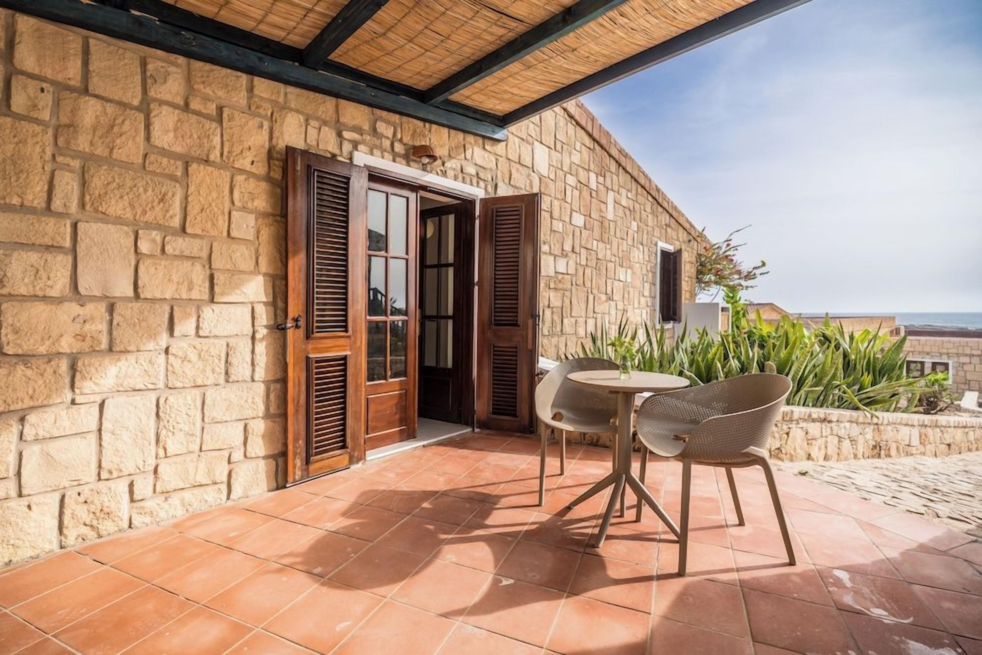 Ein Gebäude aus Stein mit einer gefliesten Terrasse, einer Holztür und einem Tisch mit Stühlen.