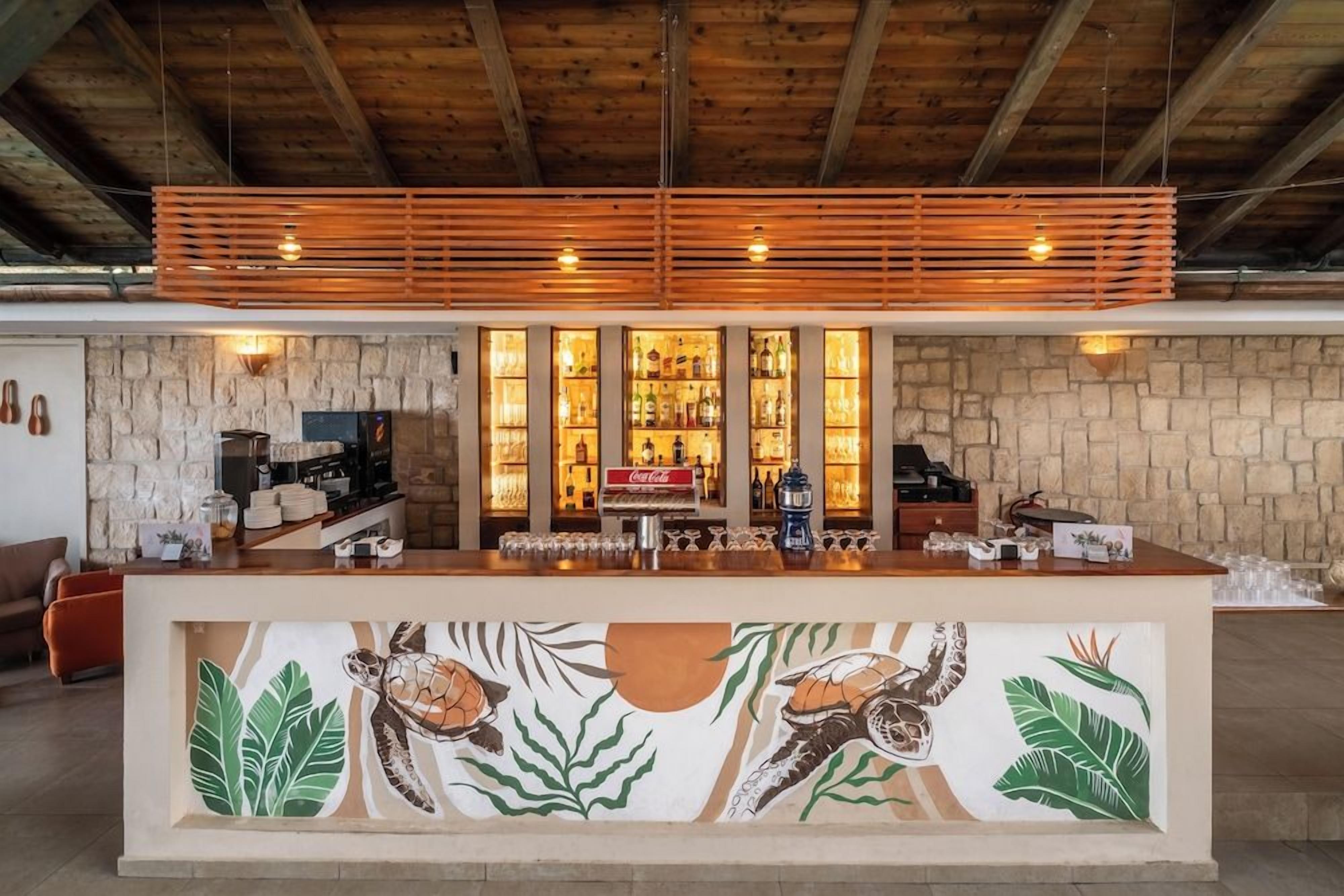A bar area with a stone wall backdrop, wooden slats overhead, and a tiled mural of sea turtles.