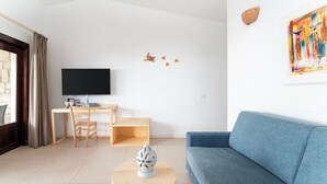 A modern living room with a blue sofa, a wooden coffee table, a TV, and a desk with a chair. - Ahg Marine Club Beach Resort (Boa Vista)