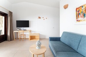 A modern living room with a blue sofa, a wooden coffee table, a TV, and a desk with a chair. - Ahg Marine Club Beach Resort (Boa Vista)