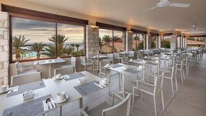 A spacious outdoor dining area with multiple tables and chairs, large windows offering a view of palm trees and a distant landscape. - Ahg Marine Club Beach Resort (Boa Vista)