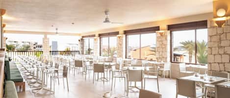 Un amplio comedor interior con varias mesas y sillas, ventanas grandes y una pared de acento de piedra.