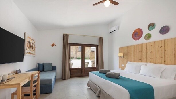 A hotel room with a bed, a desk with a chair, a sofa, a television, and a view of the outside. - Ahg Marine Club Beach Resort (Boa Vista)