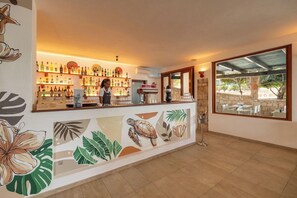 Zona de bar con un cantinero, estantes llenos de botellas de licor y un mural con hojas tropicales y una tortuga.