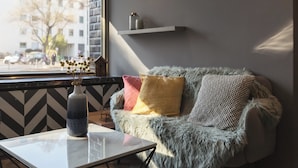 A cozy room with a sofa, a vase with flowers, a coffee table, and a window with a view of buildings and trees.
