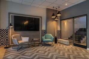 A modern interior with a large flat-screen TV, two chairs, pendant lighting, a radiator, and a patterned floor. - Yggotel Ravn (Berlin)