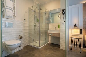 A modern bathroom with a glass-enclosed shower, a toilet, a sink, and a small table with a lamp. - Yggotel Ravn (Berlin)