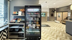 A modern hotel lobby with a vending machine stocked with beverages, a reception desk, and a patterned floor.