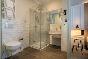 A modern bathroom with a glass-enclosed shower, a toilet, a sink, and a mirror. - Yggotel Ravn (Berlin)