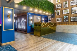 A reception area with a blue wall, a green wall with a plant, and framed pictures on the wall. - Hotel Faranda Collection Cali (Cali)
