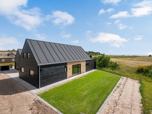 Ein modernes Haus mit Satteldach, einer großen Grünfläche vor der Fassade und Blick ins Grüne.