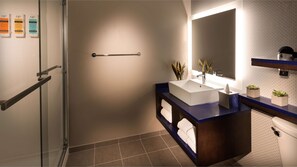 Ein modernes Badezimmer mit Duschkabine aus Glas, einem Waschbecken mit Spiegel darüber und einem Handtuchhalter.