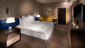 Ein Hotelzimmer mit Bett, Nachttischen, einer Lampe, einem Fernseher, einer Tür und einer Wand mit geometrischem Muster.