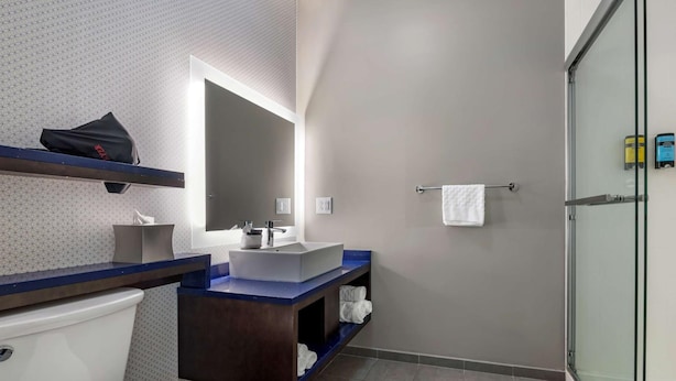 A modern bathroom with a toilet, sink, mirror, and shower. - Glo Best Western Lexington (Lexington)