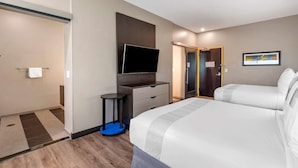 A hotel room with a bed, a TV, a small table, and a door leading to a bathroom. - Glo Best Western Lexington (Lexington)