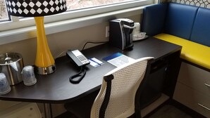A small, compact workspace with a desk, a telephone, a coffee machine, and a window with a view of trees. - Glo Best Western Lexington (Lexington)