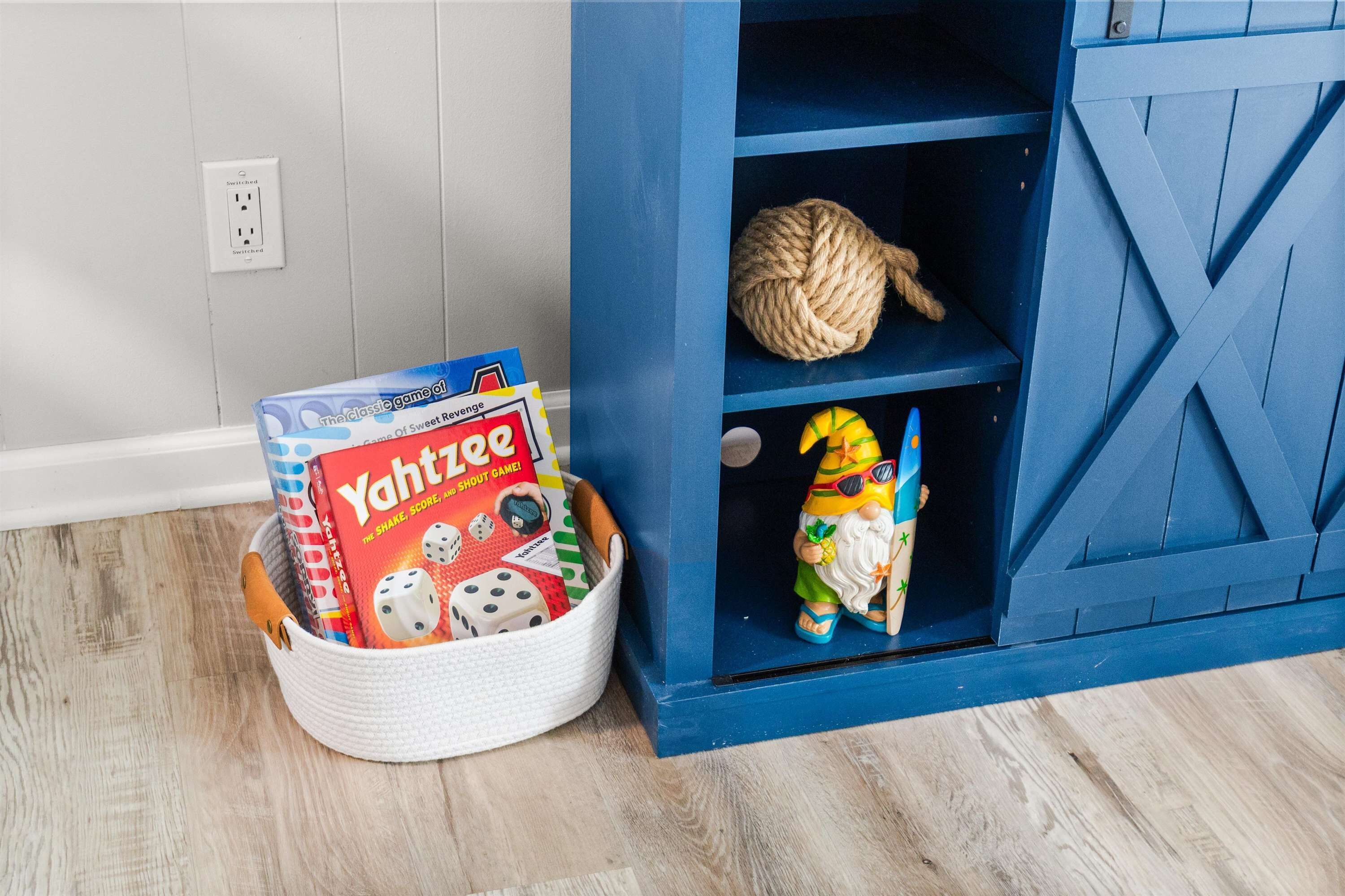 A basket with board games and a shelf with a rope and a figurine.