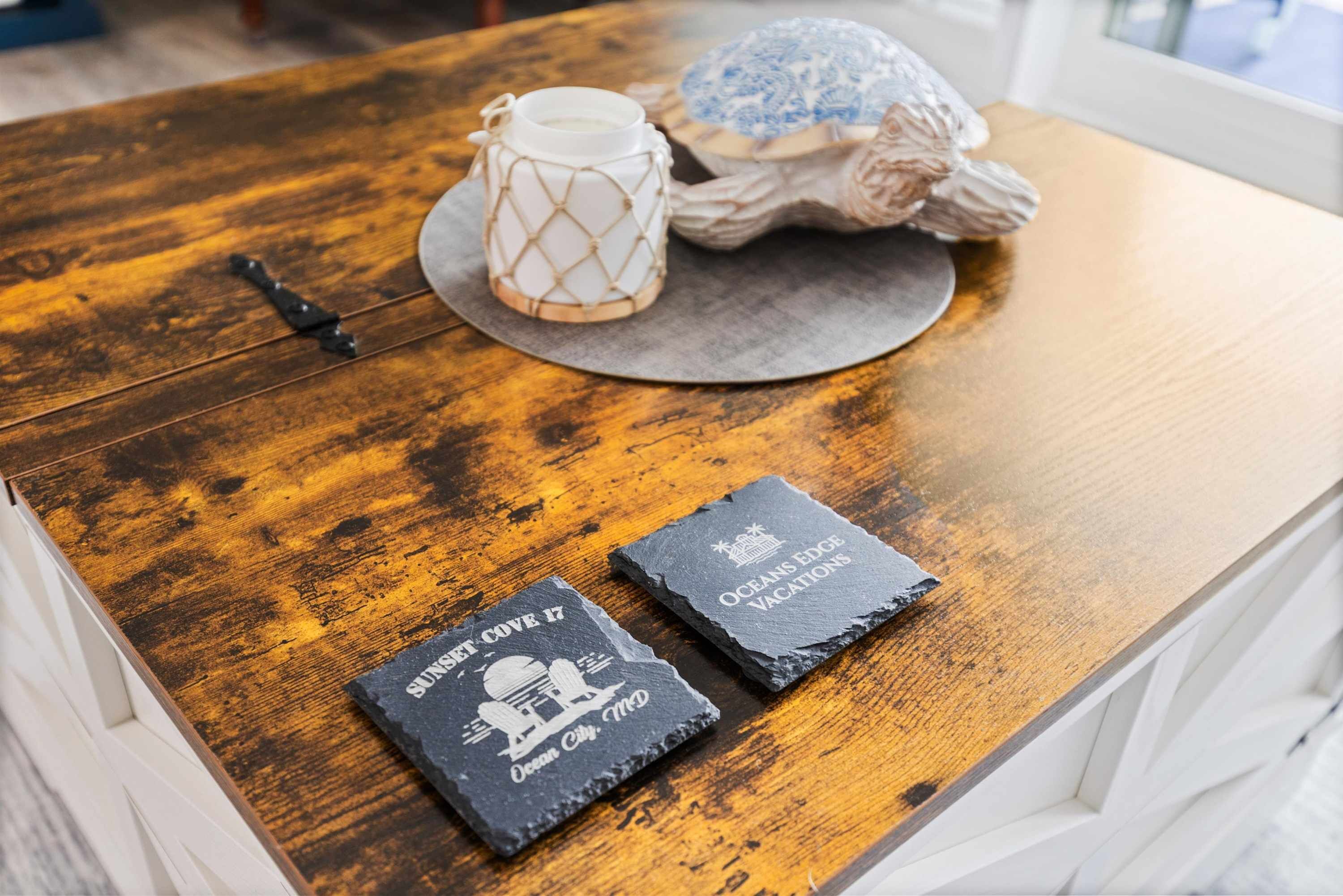 Taula de fusta amb una gerra blanca, un objecte decoratiu i dos posavasos de pissarra amb text.