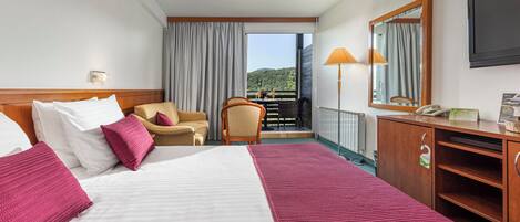 A hotel room with a bed, a desk, a chair, a balcony with a view, and a mirror.