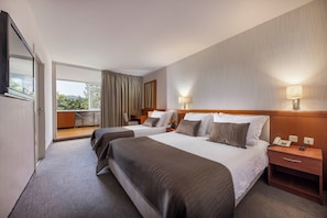 Ein Hotelzimmer mit zwei Betten, einem Balkon, einem Holz-Kopfteil, Nachttischlampen und einem Telefon auf dem Nachttisch.