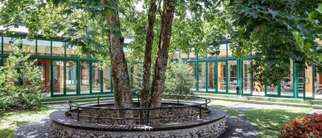 A circular stone garden with trees, surrounded by a glass building with green frames.