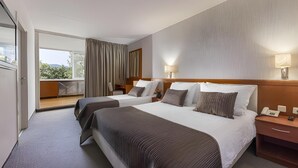 A hotel room with two beds, a balcony, and a view of greenery.