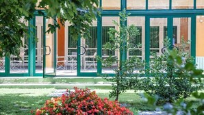 A building with large glass doors, outdoor seating, and a green frame.