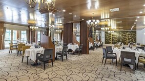 En restaurang med flera bord, kristallkronor och en mönstrad matta.