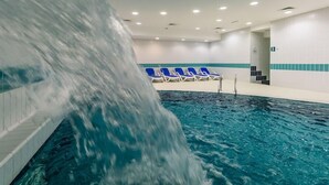 A swimming pool with a waterfall feature, blue lounge chairs, and a tiled wall with a blue stripe.