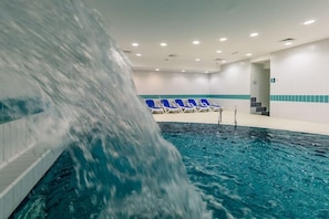 Ein Pool mit Wasserfall, blauen Liegestühlen und einer mit einer blauen Linie befliessten Wand.