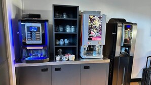 Una estación autoservicio de bebidas con una cafetera, un dispensador de agua y un refrigerador.