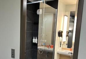 A modern bathroom with a glass-enclosed shower, a sink, and a hairdryer mounted on the wall. - B&B Hotel Le Havre Centre (Le Havre)