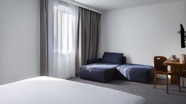 A hotel room with a bed, a sofa, a chair, a small table, and a window with curtains. - B&B Hotel Le Havre Centre (Le Havre)