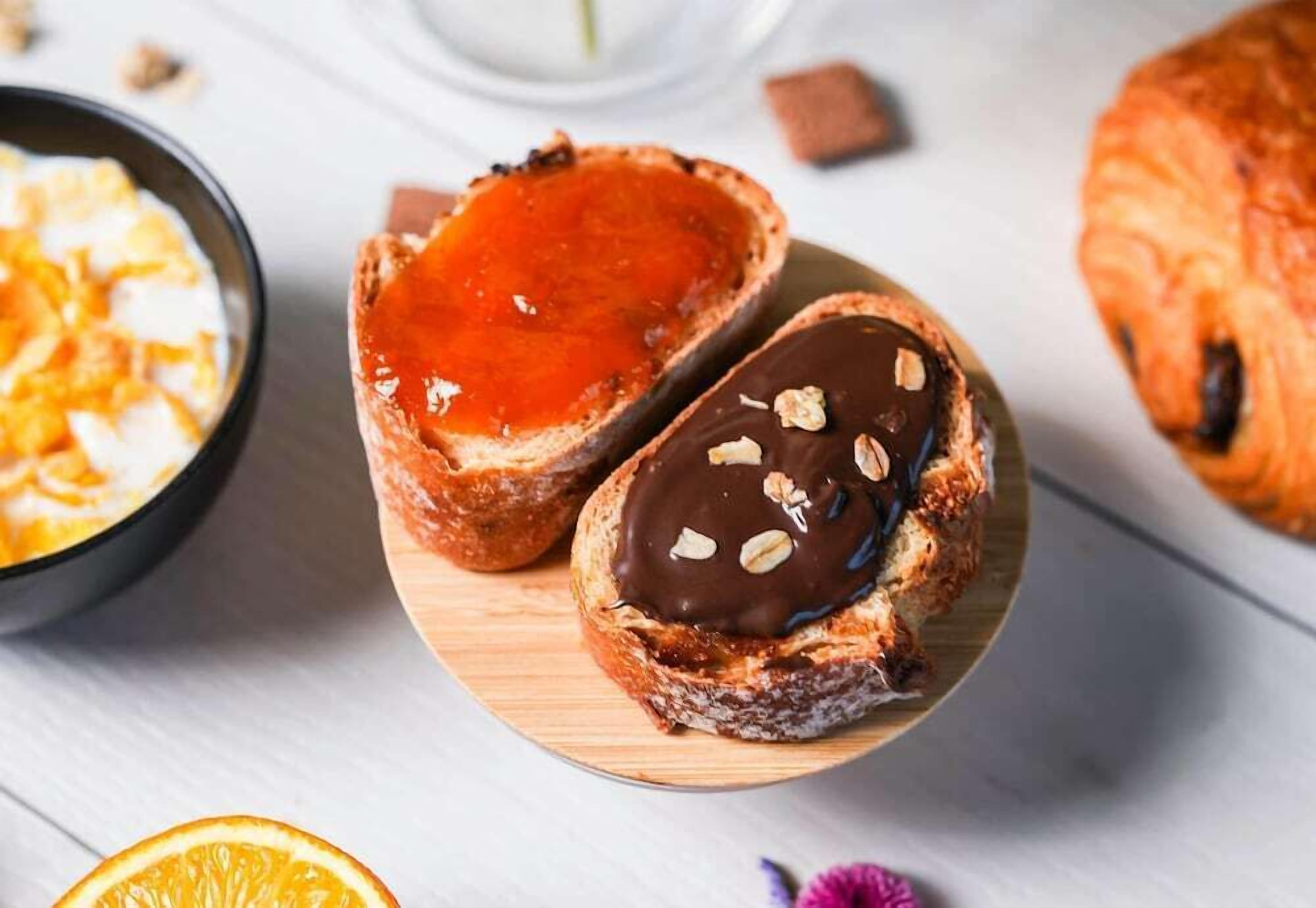 Two pastries on a wooden board, one with a red filling and the other with chocolate and nuts.