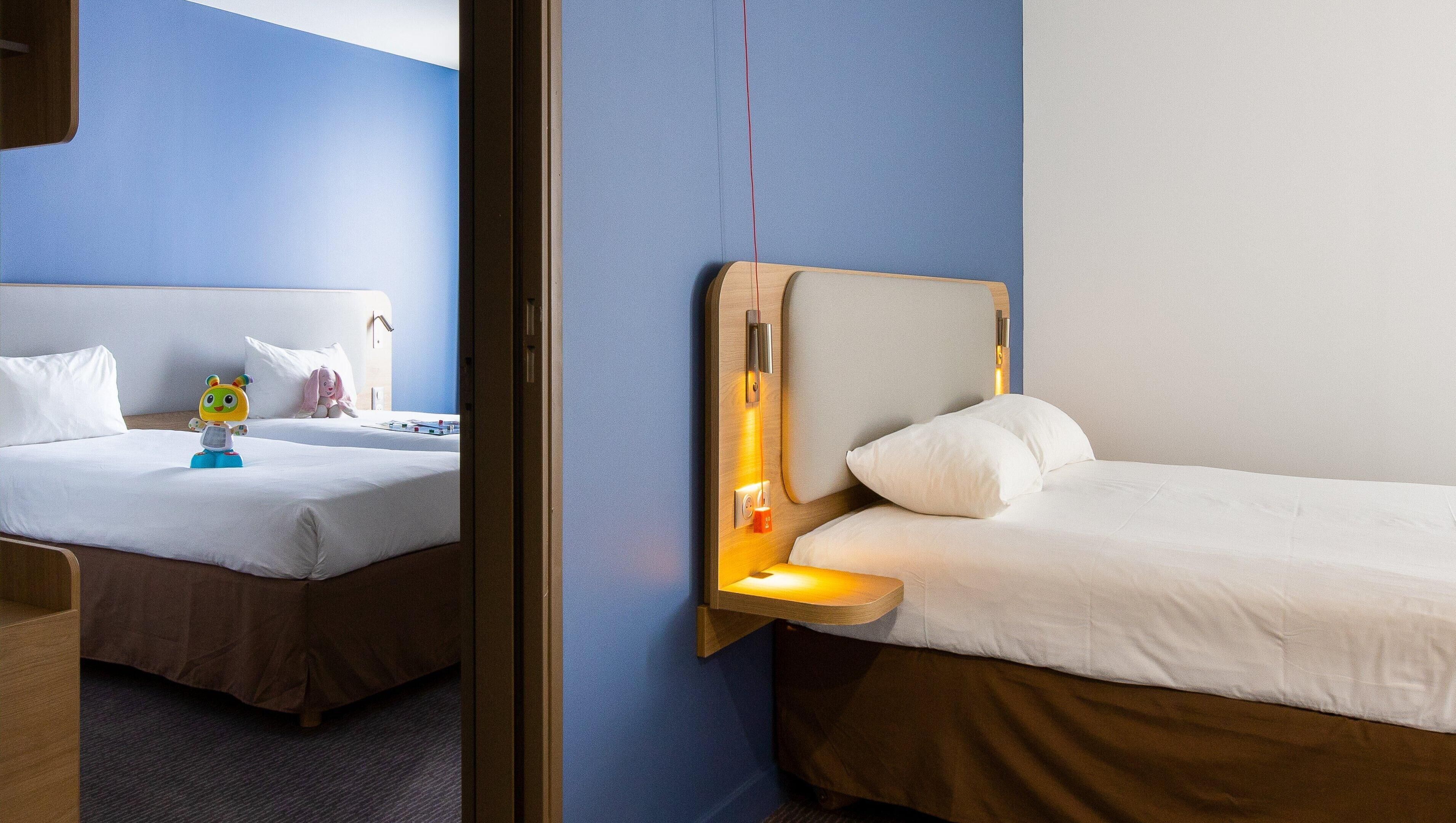 Une chambre d’hôtel avec deux lits, une tête de lit en bois et une table de chevet avec une lampe.