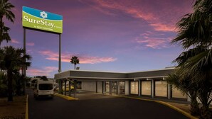 A hotel entrance with a SureStay sign, a covered parking area, and a van parked outside. - Laredo Hotel (Laredo)