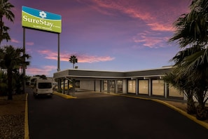 A hotel entrance with a SureStay sign, a covered parking area, and a van parked outside. - Laredo Hotel (Laredo)