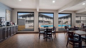 A modern hotel room with a kitchen area, dining space with tables and chairs, and large windows offering views of a pool and building exterior. - Laredo Hotel (Laredo)