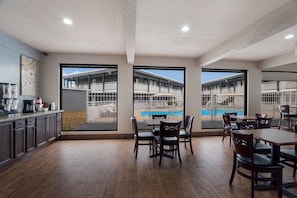 A modern hotel room with a kitchen area, dining space with tables and chairs, and large windows offering views of a pool and building exterior. - Laredo Hotel (Laredo)