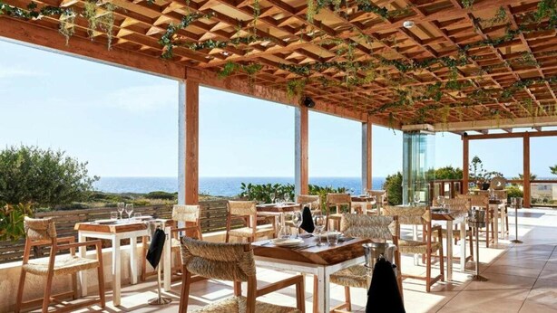 An outdoor dining area with wooden tables and chairs, a pergola with greenery, and a view of the sea. - Vasia Sea Retreat - Adults Only (Agios Nikolaos)