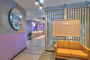 A reception area with a purple wall, a round mirror, a wooden partition, and a yellow sofa. - Intercityhotel Kassel (Kassel)