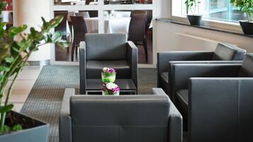 Eine moderne Lounge mit Ledersitzgelegenheiten, einem kleinen Tisch mit Blumenarrangement und Blick auf ein Restaurant im Hintergrund.