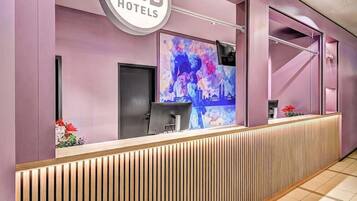 Ein moderner Empfangstresen, ein großes Schild für B&B Hotels und ein farbenfrohes, abstraktes Gemälde an der Wand.