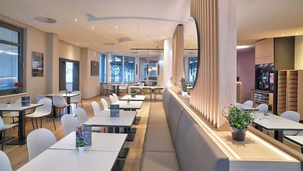 A modern dining area with tables, chairs, and a long bench. - Intercityhotel Kassel (Kassel)