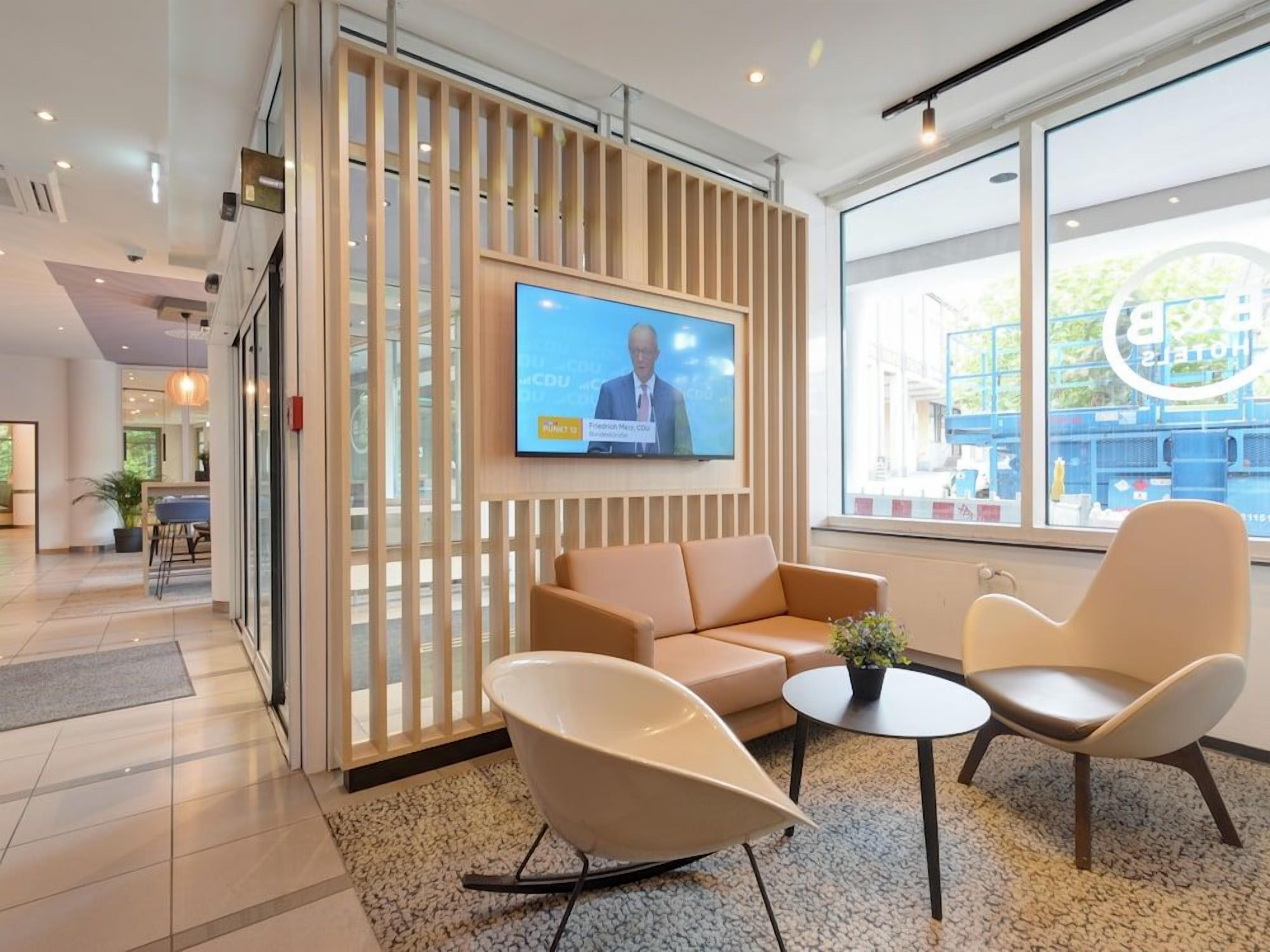 A modern hotel lobby with a television, seating area, and large windows.